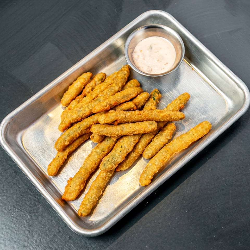 Golden fried pickle spears on a metal tray with a side of creamy dipping sauce.