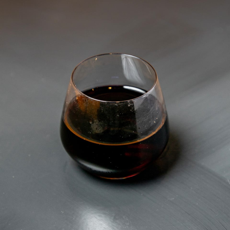 A dark beverage in a stemless glass sits on a dark gray surface.