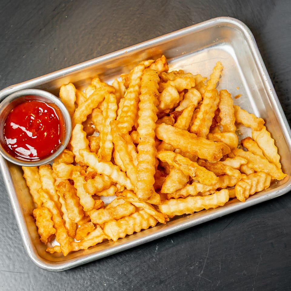 A metal tray filled with golden, crispy crinkle-cut fries and a side of ketchup.