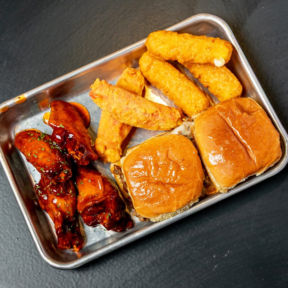 A metal tray with BBQ chicken wings, mozzarella sticks, and two sliders.