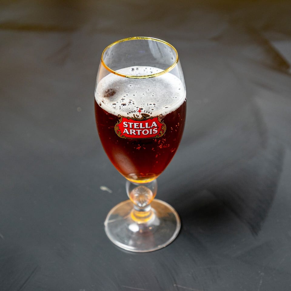 A Stella Artois beer in a branded chalice glass with a golden rim, on a dark surface.